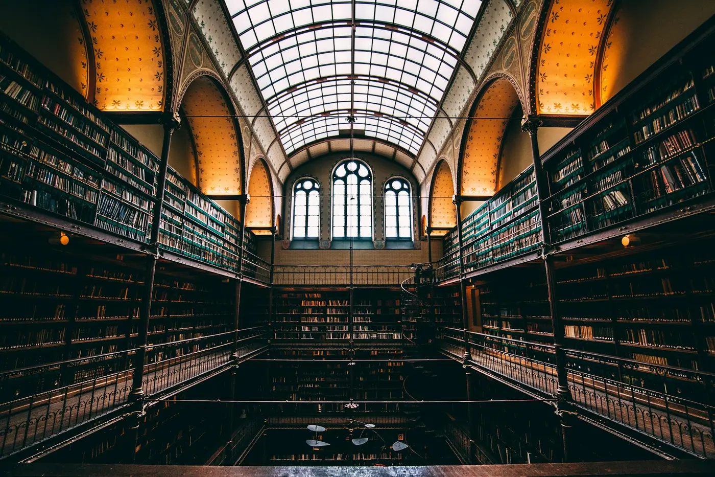 A vaulted nineteenth century library hall with tiered galleries of books rising to a glazed barrel roof.